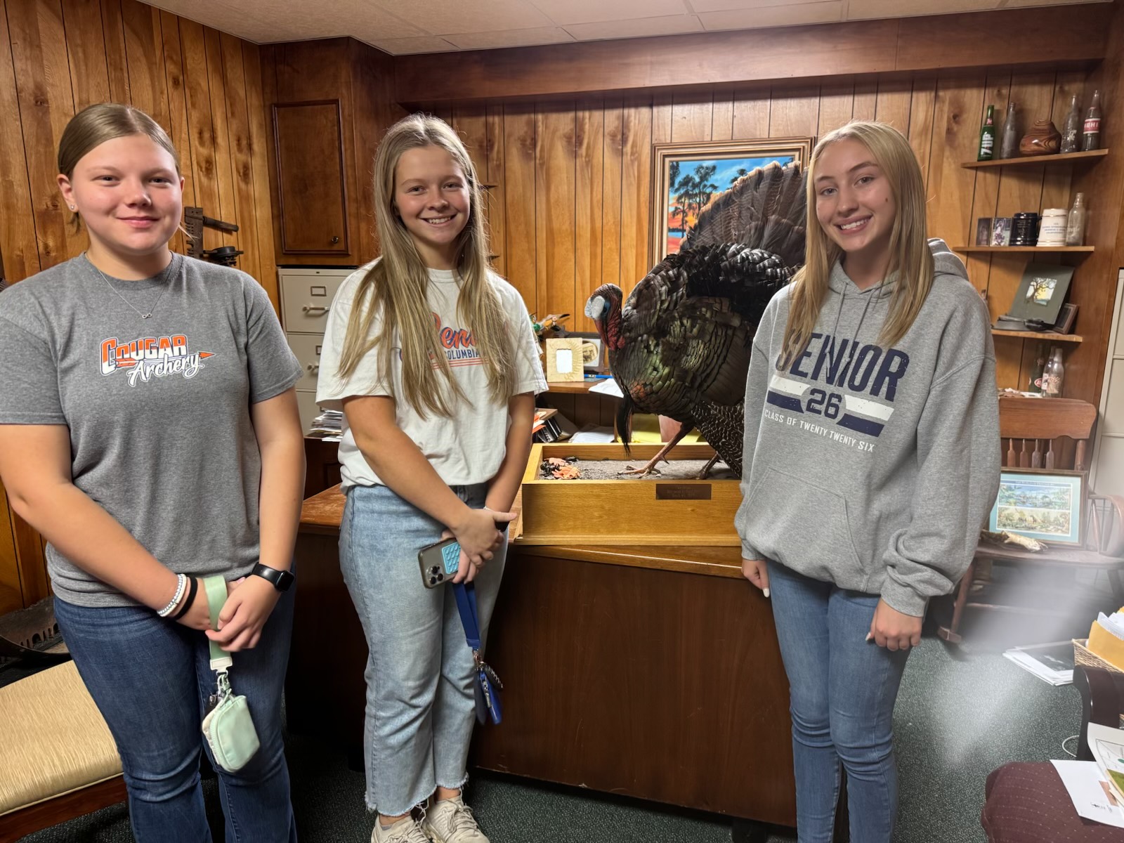 Three high-school students standing beside the museum's wild turkey mount